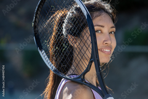 Asian female tennis player holding a racket and standing on the court outside.  photo