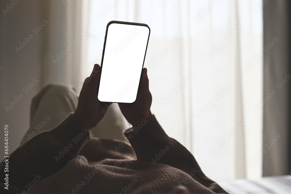 Mockup image of woman holding mobile phone with blank desktop white screen while lying on bed - obrazy, fototapety, plakaty 
