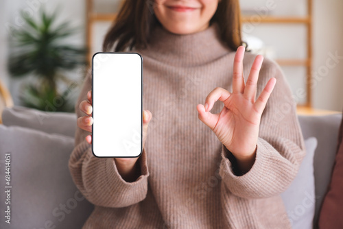 Closeup image of a young woman making okay hand sign while holding and showing a mobile phone with blank white screen photo
