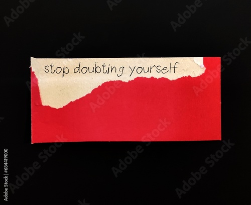 Torn red note with handwritten text STOP DOUBTING YOURSELF, concept of self-doubt, lack of confidence  mindset that hold back from succeeding leads to imposter syndrome or self sabotage photo