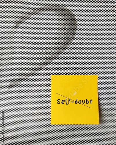 Stick yellow note on gray background with text  Self-doubt - means lacking of confidence or have a mindset that holds you back from succeeding leads to imposter syndrome or self-sabotage photo