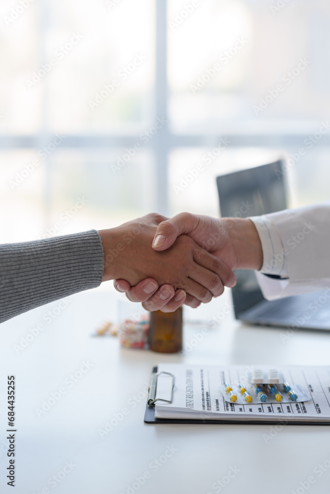 Medical service worker or doctor, pharmacist shaking hands with female medical patient at the table in clinic after giving advice on how to take medicine to the patient. Health care service concept. - obrazy, fototapety, plakaty 