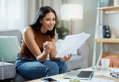 Happy woman, laptop and documents on sofa for finance, expenses or paying bills in living room at home. Female person smile with paperwork for good budget, investments or financial plan at house