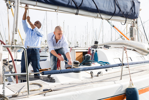 Two men in blue shirts and jeans working on sailing yacht in the port