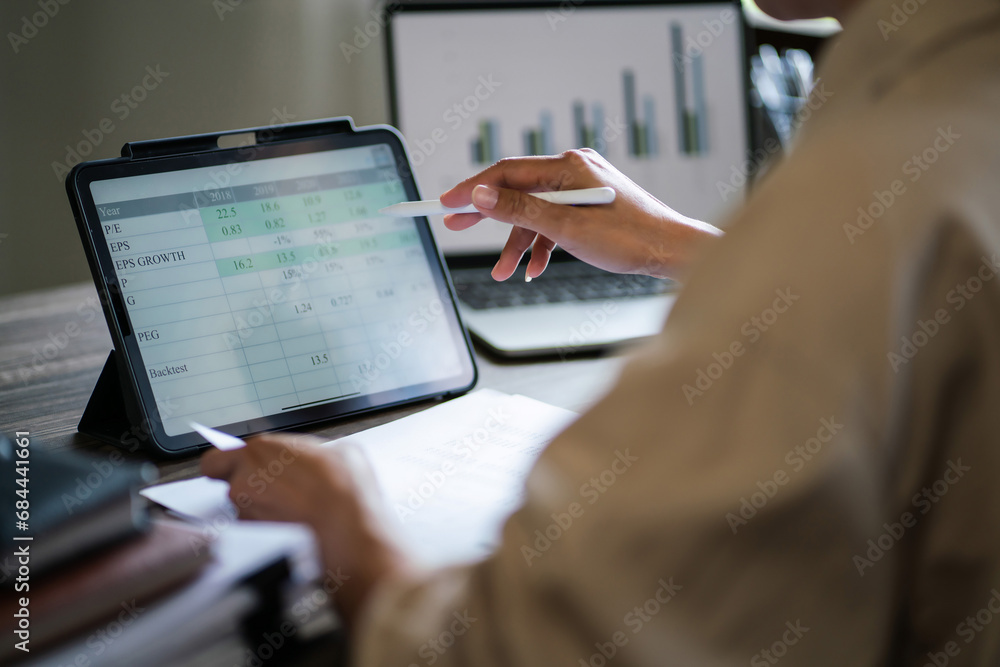 Fototapeta premium Female entrepreneur reading data on tablet and writing notes while working about finance of startup