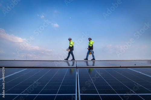 Engineers walking on roof inspect and check solar cell panel by hold equipment box and radio communication ,solar cell is smart grid ecology energy sunlight alternative power factory concept