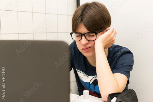 A tired student with a laptop is doing homework, preparing for exams.