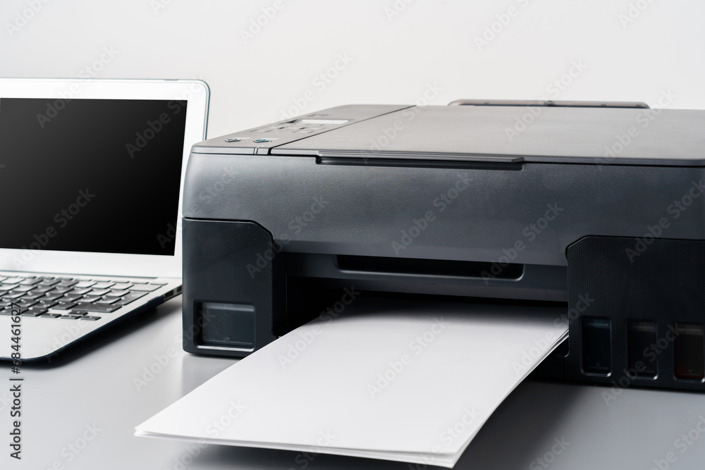 Printer and laptop on grey table in office Printer and laptop on grey table in office