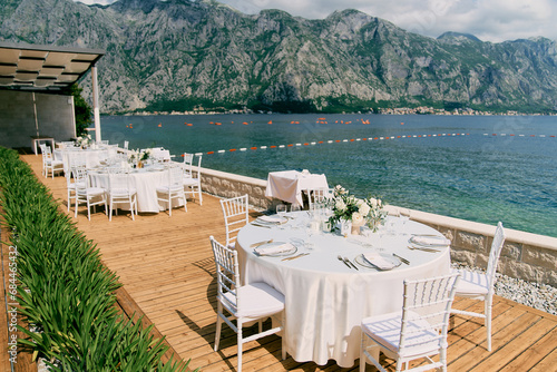 Round tables set on a wooden deck in a garden overlooking the sea photo