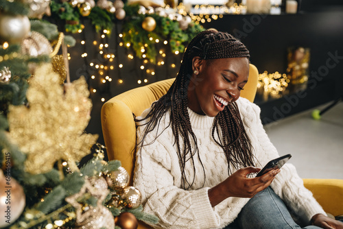 Young beautiful African woman using her phone at home decorated for Christmas season photo