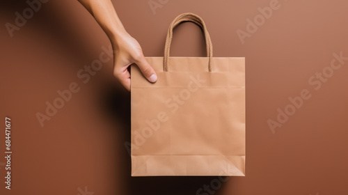 Close up female holds in hand white clear empty blank craft paper gift bag for purchases after shopping isolated on pastel biege background. Delivery concept advertising mock.