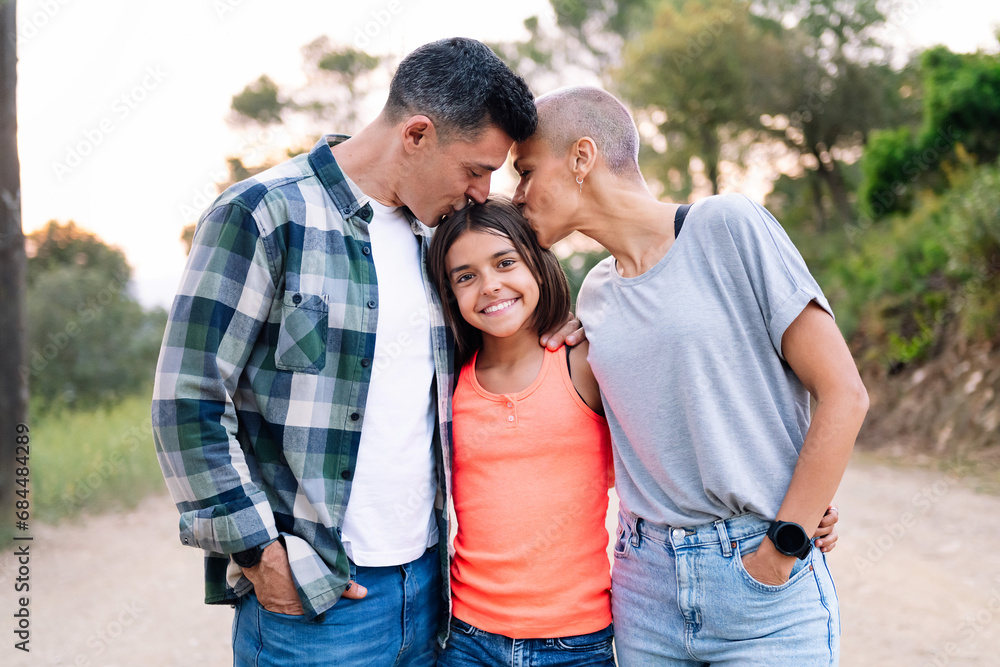 portrait in the countryside of a father and mother kissing their daughter who smiles happily looking at camera, concept of active tourism in nature and family outdoors activities portrait in the countryside of a father and mother kissing their daughter who smiles happily looking at camera, concept of active tourism in nature and family outdoors activities
