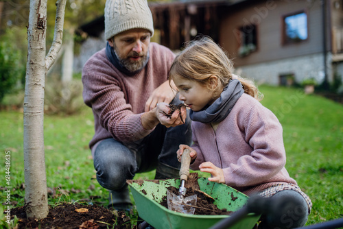 Girl and father planting tree in garden in the spring, using compost. Girl smelling compost, learning abou composting. Concept of sustainable gardening family gardening. photo