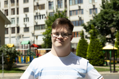 A boy with Down syndrome poses against the background of a summer city