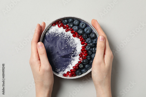 Bowl with smoothie in female hands on gray background, top view
