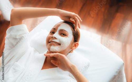 Serene daylight ambiance of spa salon, top view woman lying on massage table smiling and rejuvenating with face cream spa massage. Facial skin spa treatment and beauty care concept. Quiescent