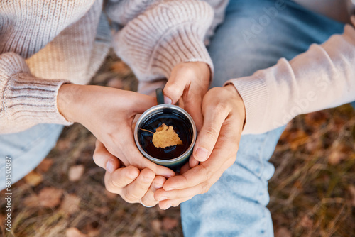 Two hands, male and female, hold a metallic cup of tea in autumn in nature. A small yellow birch leaf floats in a cup. Lifestyle, love, comfort content photo