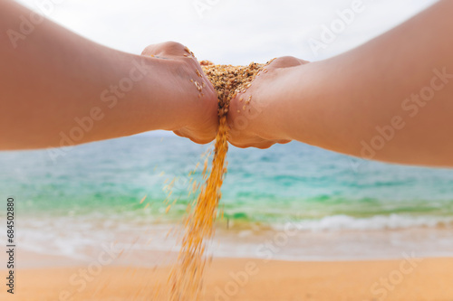 hand releases the falling sand. Fine sand flows through your fingers against the backdrop of the sea. Summer beach holiday and time passing concept #684502880