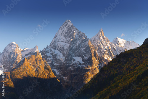 Sharp mountain peaks partially covered with snow and surrounded by rays of sun under a picturesque blue sky after dark, sunset or sunrise in the mountains in winter