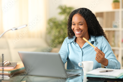 Happy black tele worker eating snack at home