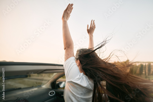 A Happy Woman Enjoying a Summer Road Trip in a Convertible Car. She Raises Her Hands Up in the Air and Feels the Freedom of Travel and Vacation.