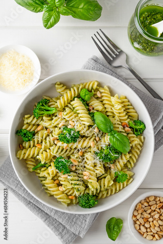 Vegetarian pasta with pesto sauce, broccoli, parmesan cheese and pine nuts on a white wooden background. Healthy food.