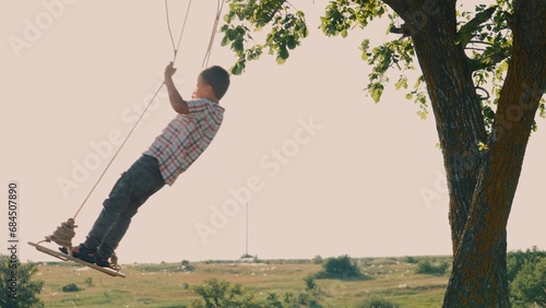 Active boy energetically swinging on homemade swing spending time in nature