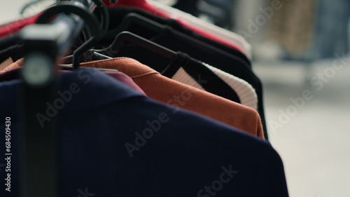 Empty premium fashion boutique with elegant clothes on racks, close up shot. High street men blazers and other garments on hangers in trendy clothing store in shopping center