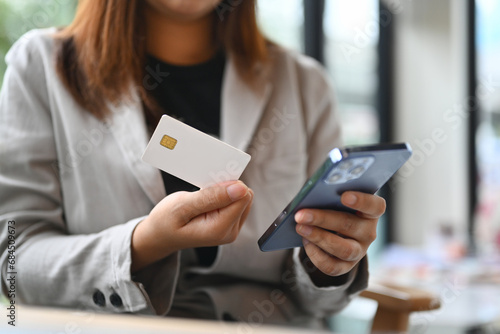 Young woman hand holding credit bank card and using mobile phone for shopping online