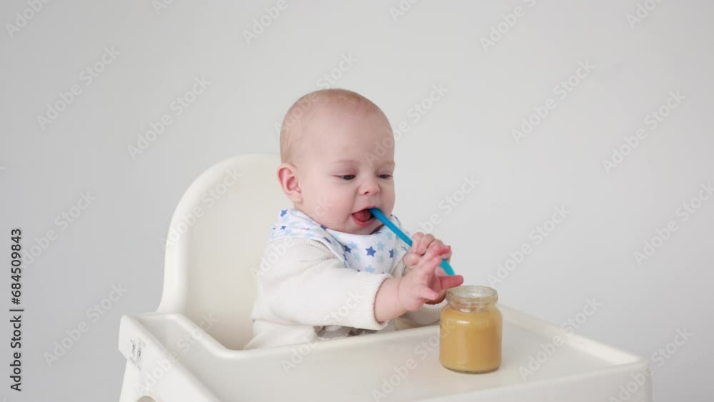 4k, cute baby girl sitting on a feeding chair nibbling a silicone baby spoon looking at the camera, the concept of introducing complementary foods for babies 4k, cute baby girl sitting on a feeding chair nibbling a silicone baby spoon looking at the camera, the concept of introducing complementary foods for babies