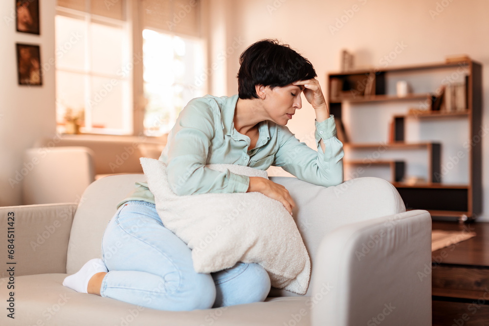 Brunette lady sitting exhausted and distraught from headache at home Brunette lady sitting exhausted and distraught from headache at home