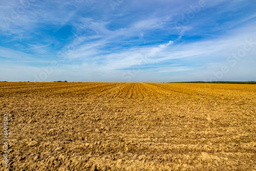Panoramic view of a agricultural field after harvesting against a hazy blue sky, horizon in background, landscape of Belgian farmland, sunny summer day in Vise, Belgium