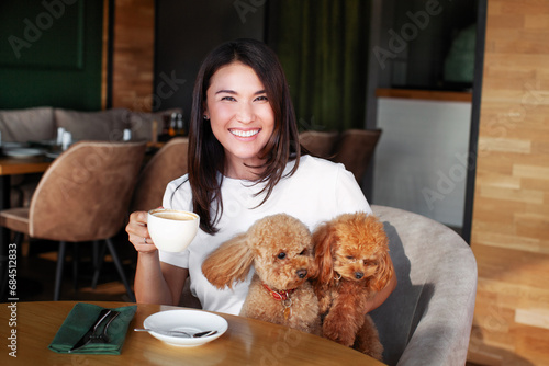 Photography Portrait of smiling woman with two small dogs poodles sitting at table in restaurant with cup of coffee