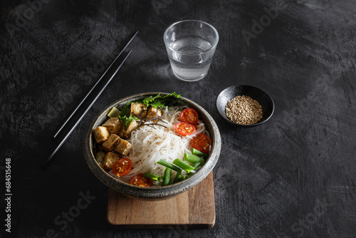 Bowl of vegan Tom kha kai soup with tofu, tomatoes, salad, rice noodles, sesame seeds and scallion