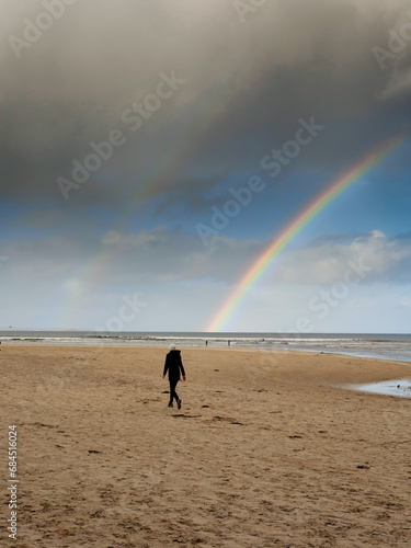 Nature scene with beach, ocean and cloudy sky with rainbow. Silhouette of people walking on the sand. Rich saturated colors. Nature wonder scene. West of Ireland.