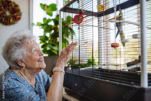 Happy senior woman looking at bird in cage at home photo