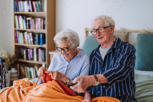 Happy senior woman knitting with man holding remote and watching TV at home photo