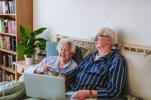 Smiling senior man and woman sitting with laptop on bed at home photo