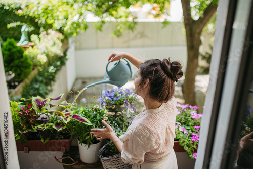 Woman watering flowers, taking care of plants on balcony photo