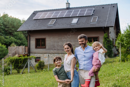 Happy family standing in front their family house with solar panels on the roof photo
