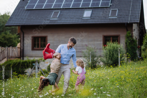 Father and daughters having fun in front their family house with solar panels on the roof photo