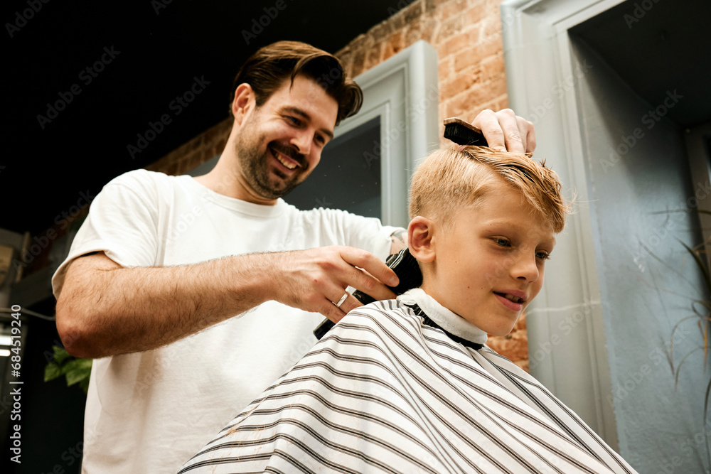 Smiling barber cutting customer's hair with electric razor at salon Smiling barber cutting customer's hair with electric razor at salon