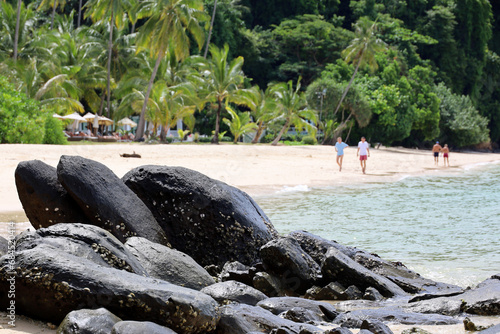 Tropical sandy beach with big stones on palm trees background. People on sea resort, vacation concept