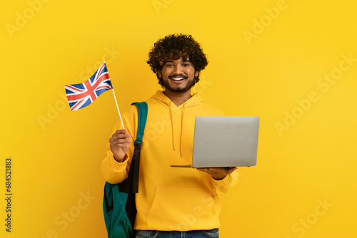 Happy young indian guy holding laptop and flag of UK photo