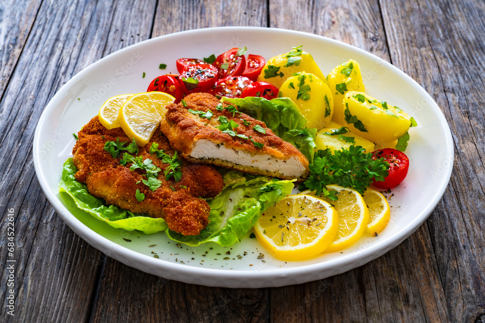 Crispy breaded fried chicken cutlet with fresh vegetables and boiled potatoes on wooden table
Crispy breaded fried chicken cutlet with fresh vegetables and boiled potatoes on wooden table
