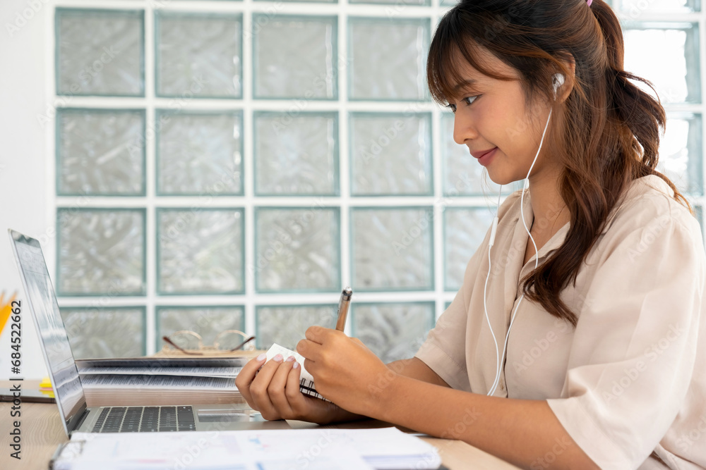 Young student taking notes while studying online. Young student taking notes while studying online.