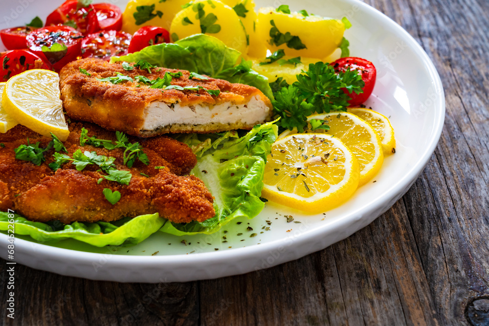 Crispy breaded fried chicken cutlet with fresh vegetables and boiled potatoes on wooden table
Crispy breaded fried chicken cutlet with fresh vegetables and boiled potatoes on wooden table