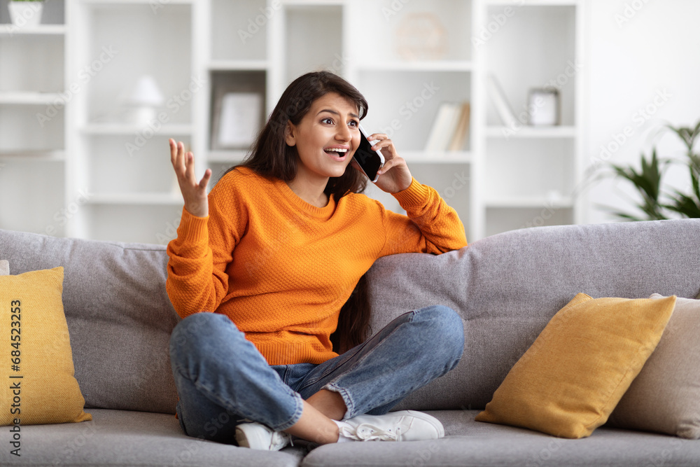 Emotional pretty young indian woman talking on phone at home - obrazy, fototapety, plakaty 