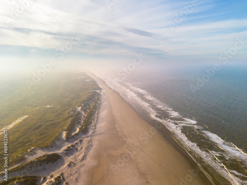 Aerial image of a golden beach with rolling waves, sand dunes and blue sky in warm sunlight on island Dutch Wadden Terschelling photo