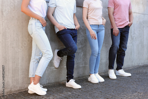 Group of people in stylish jeans near grey wall outdoors, closeup